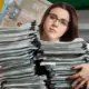 Mulher cansada com diversos cadernos e de fundo a bandeira do Brasil com dinheiro